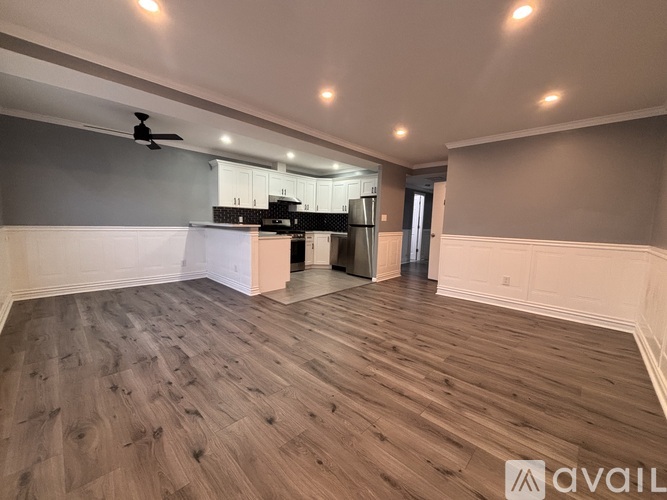 A spacious room with wooden flooring and a kitchen area in the background.