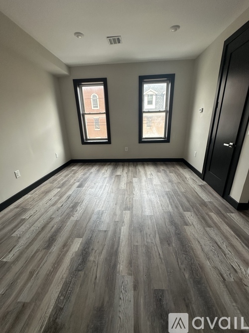 A room with wooden flooring and two windows.