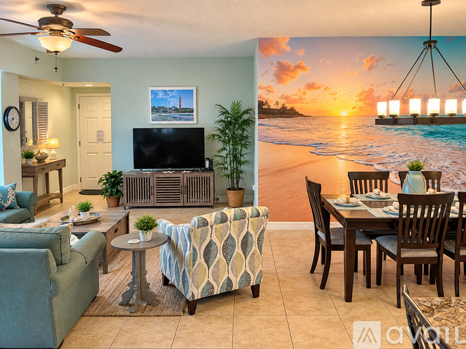 A living room with a television, a couch, a chair, a table, and a wall mural of a beach scene.