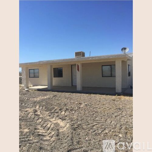 A small house with a flat roof and a satellite dish on top is situated in a barren landscape.