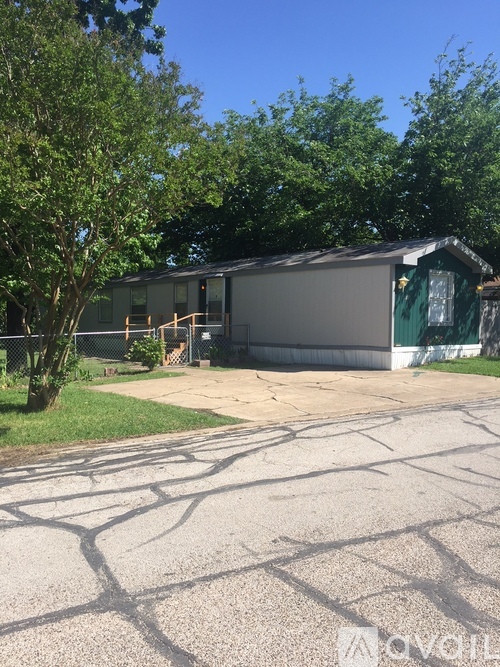 A grey building with a green door is surrounded by trees.