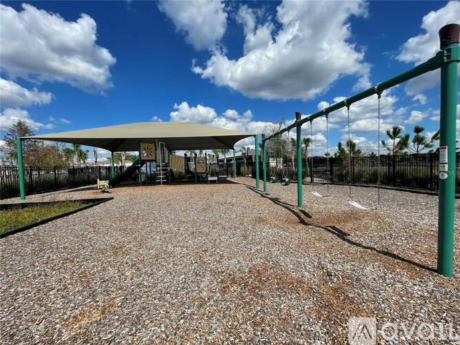 A playground with a swing set and a green fence.