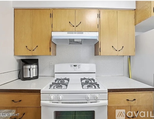 A white stove top oven with a pot on the left and wooden cabinets above it.