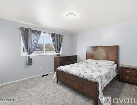 A bedroom with a large bed and a window with curtains.