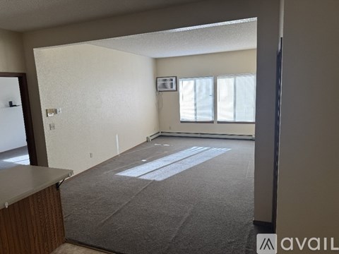 A spacious living room with a carpeted floor and a window with blinds.