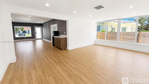 A spacious room with wooden flooring and a large window overlooking a residential area.
