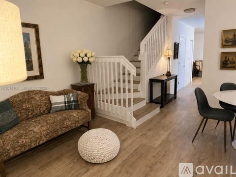 A living room with a brown patterned couch, a white ottoman, and a black chair.