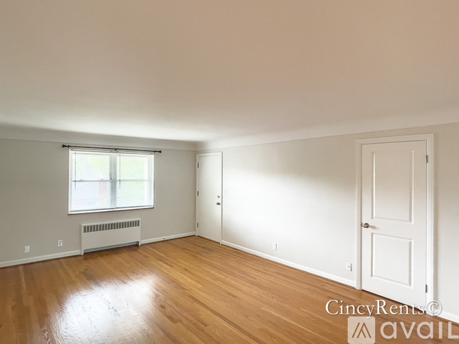 A room with wooden floors and white walls, with a window and a door.