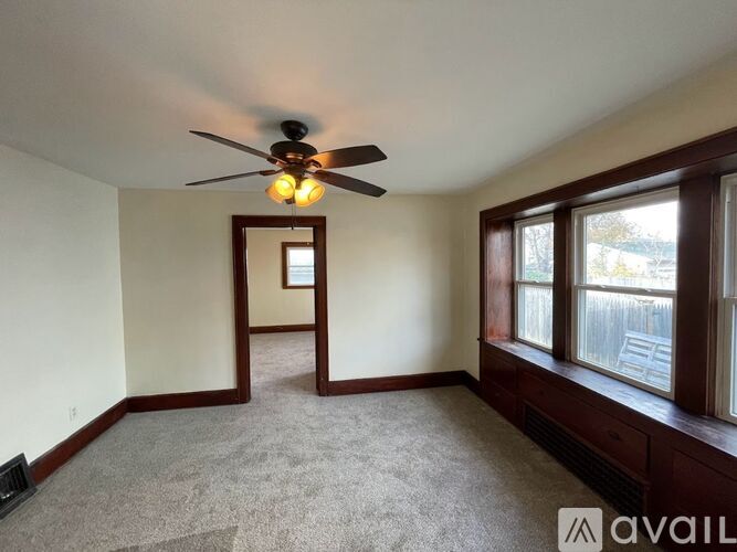 A room with a ceiling fan and a window overlooking a fence.