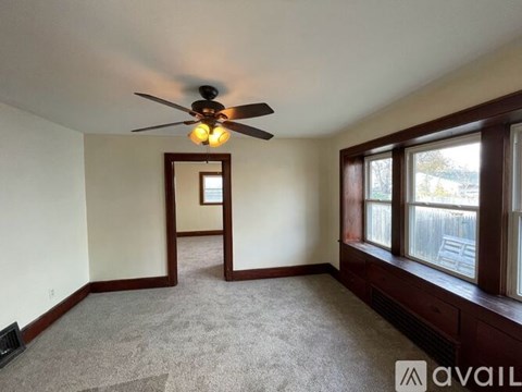 A room with a ceiling fan and a window overlooking a fence.