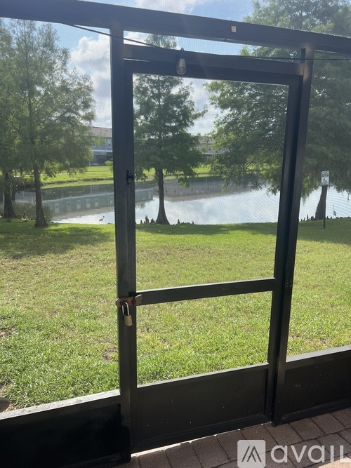 A metal gate with a lock is open, revealing a grassy area and a body of water.