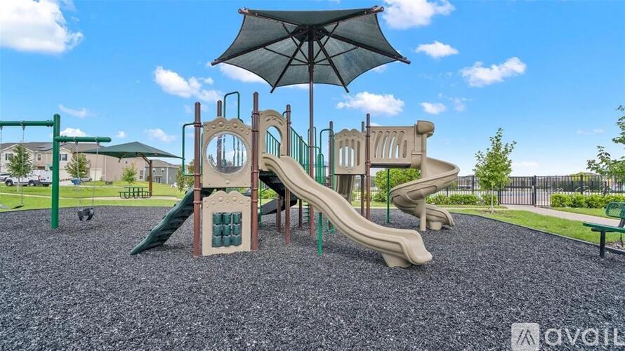 A playground with a green slide and a brown slide under a black umbrella.