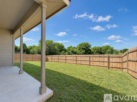 A patio with a white roof and concrete floor is surrounded by a wooden fence and green grass.