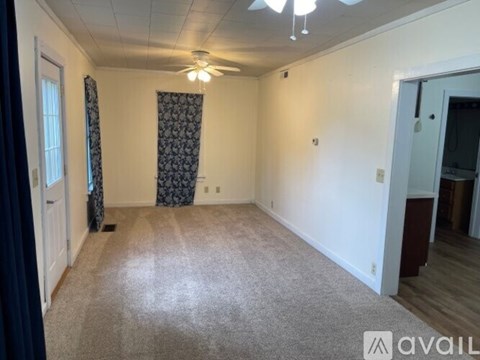 A room with a carpeted floor, a ceiling fan, and a door leading to another room.