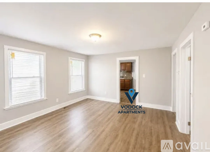 A room with wooden flooring and white walls, with a window on the left and a door on the right.