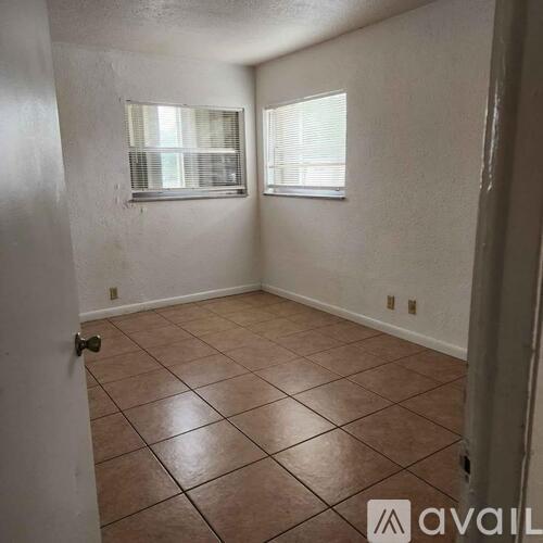 A room with brown tile flooring and two windows.