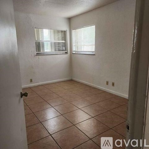 A room with brown tile flooring and two windows.