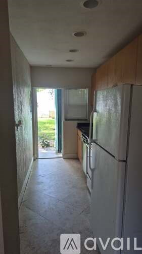 A kitchen with a refrigerator and a doorway leading to a balcony.