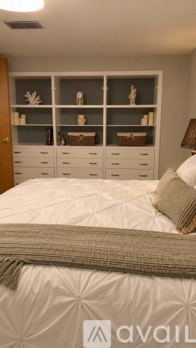 A bedroom with a bed, nightstand, and shelves with decorative items.
