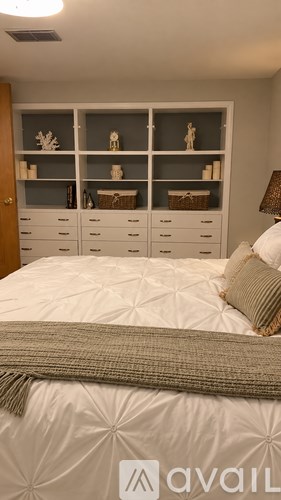 A bedroom with a bed, nightstand, and shelves with decorative items.