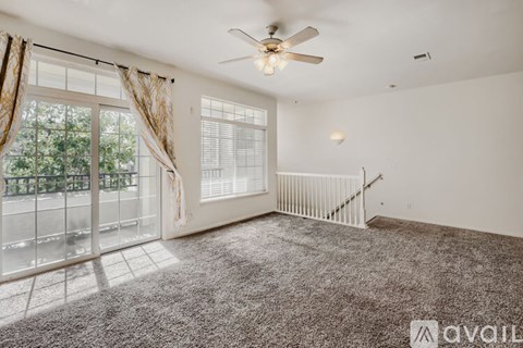 A spacious room with a fan, carpeted floor, and a staircase.