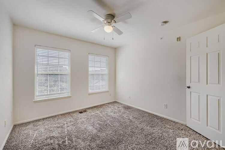 A room with a carpeted floor, a ceiling fan, and a door.