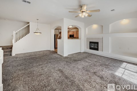 A spacious living room with a grey carpet and a ceiling fan.