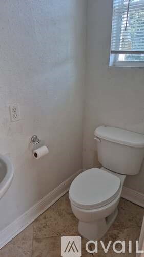 A white toilet in a bathroom with a roll of toilet paper on the wall.