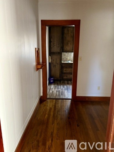 A room with wooden floors and a white wall with a doorway leading to another room.