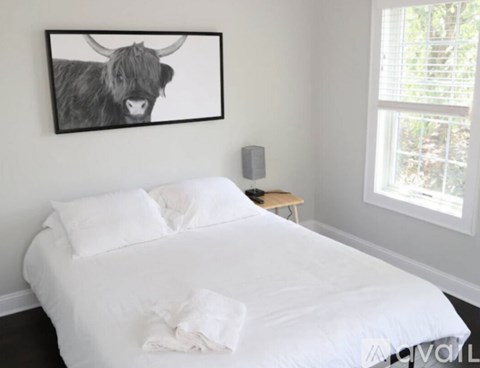 A bedroom with a white bed and a picture of a bull on the wall.