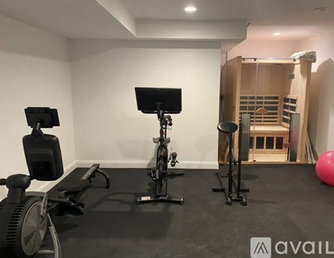 A gym room with a stationary bike, a rowing machine, and a squat rack.