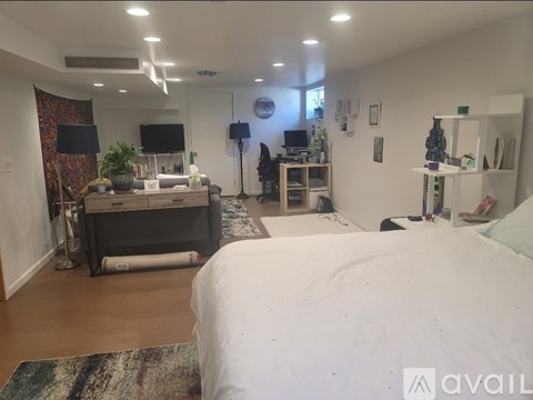 A bedroom with a large bed, a desk with a chair, and a TV on the wall.