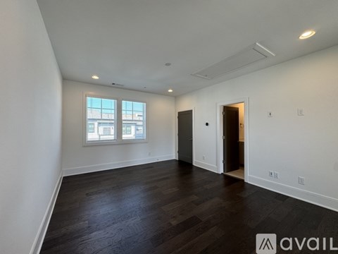 A spacious room with dark wood flooring and white walls.
