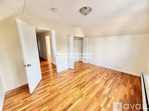 A room with wooden flooring and white walls, with a door open to another room.