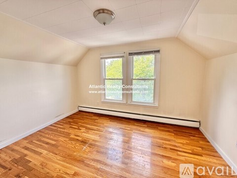 A room with wooden flooring and a window showing greenery outside.