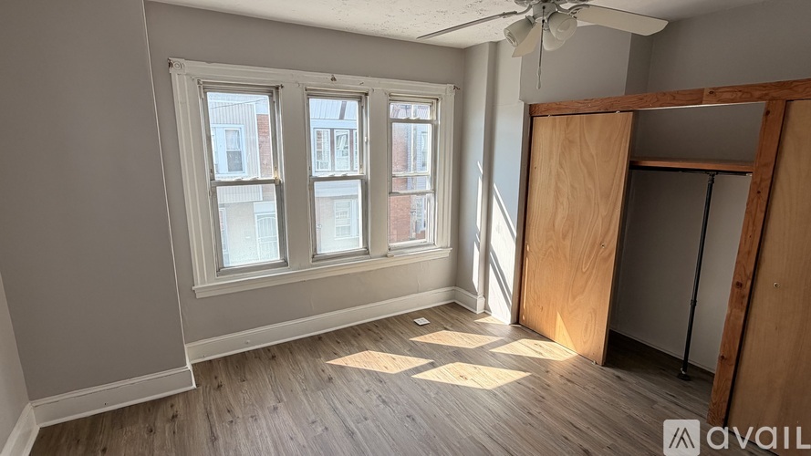 A room with a fan, wooden floors, and a window overlooking a city street.