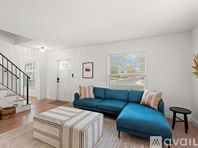 A living room with a blue couch and a striped ottoman.