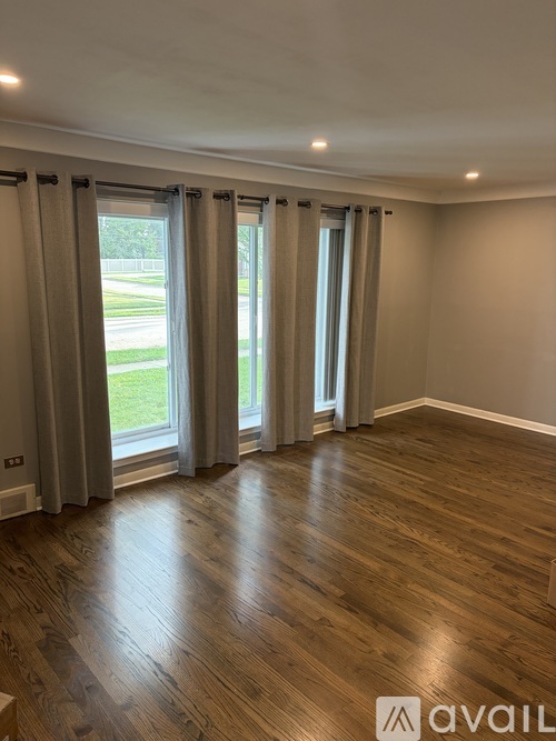 A room with wooden flooring and large windows with curtains.