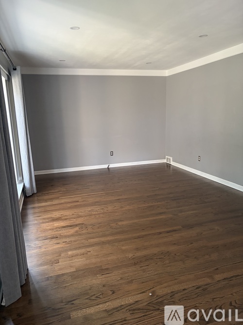 A room with wooden flooring and a window with curtains.