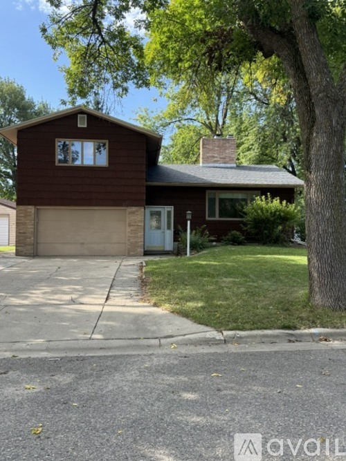 A house with a brown siding and a white door is surrounded by greenery.