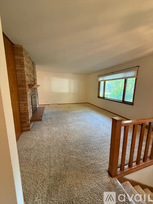 A carpeted room with a window and a wooden staircase.