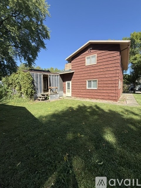 A house with a red siding and a white window is surrounded by a green lawn.
