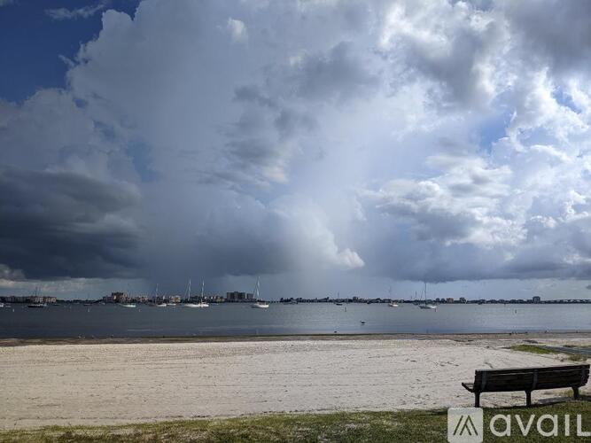 A bench with the word "AVAIL" on it sits on a beach with a cloudy sky overhead.