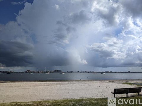A bench with the word "AVAIL" on it sits on a beach with a cloudy sky overhead.