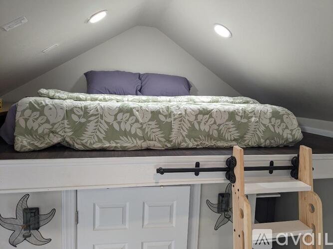 A bed with a green floral comforter and two pillows is on a platform bed with a white cabinet underneath.