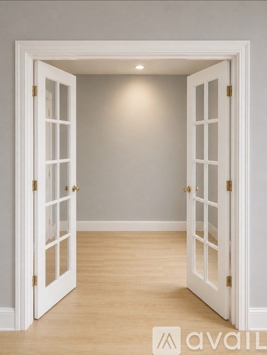 A white door with a gold handle is open to a room with wooden flooring.