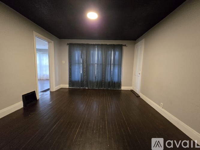 A room with wooden flooring and a window with curtains.