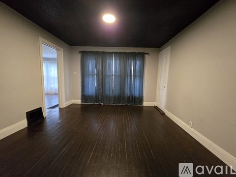 A room with wooden flooring and a window with curtains.