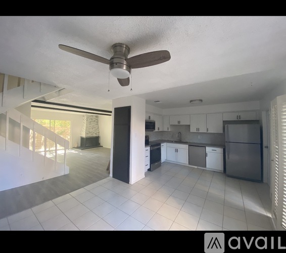A spacious kitchen and living room with a ceiling fan and white tiled floors.