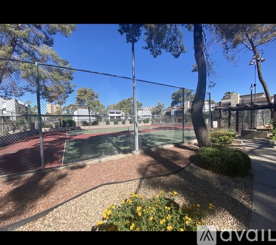A tennis court surrounded by a fence with trees and bushes.
